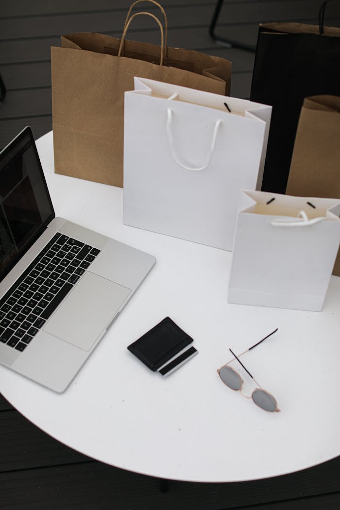 High angle view of a table with a laptop, shopping bags, wallet, and sunglasses, showcasing modern online shopping.